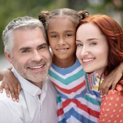 A white couple posing with their mixed race adopted daughter