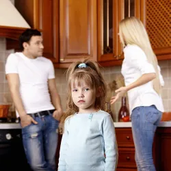 Achild standing away from her parents who are arguing with each other